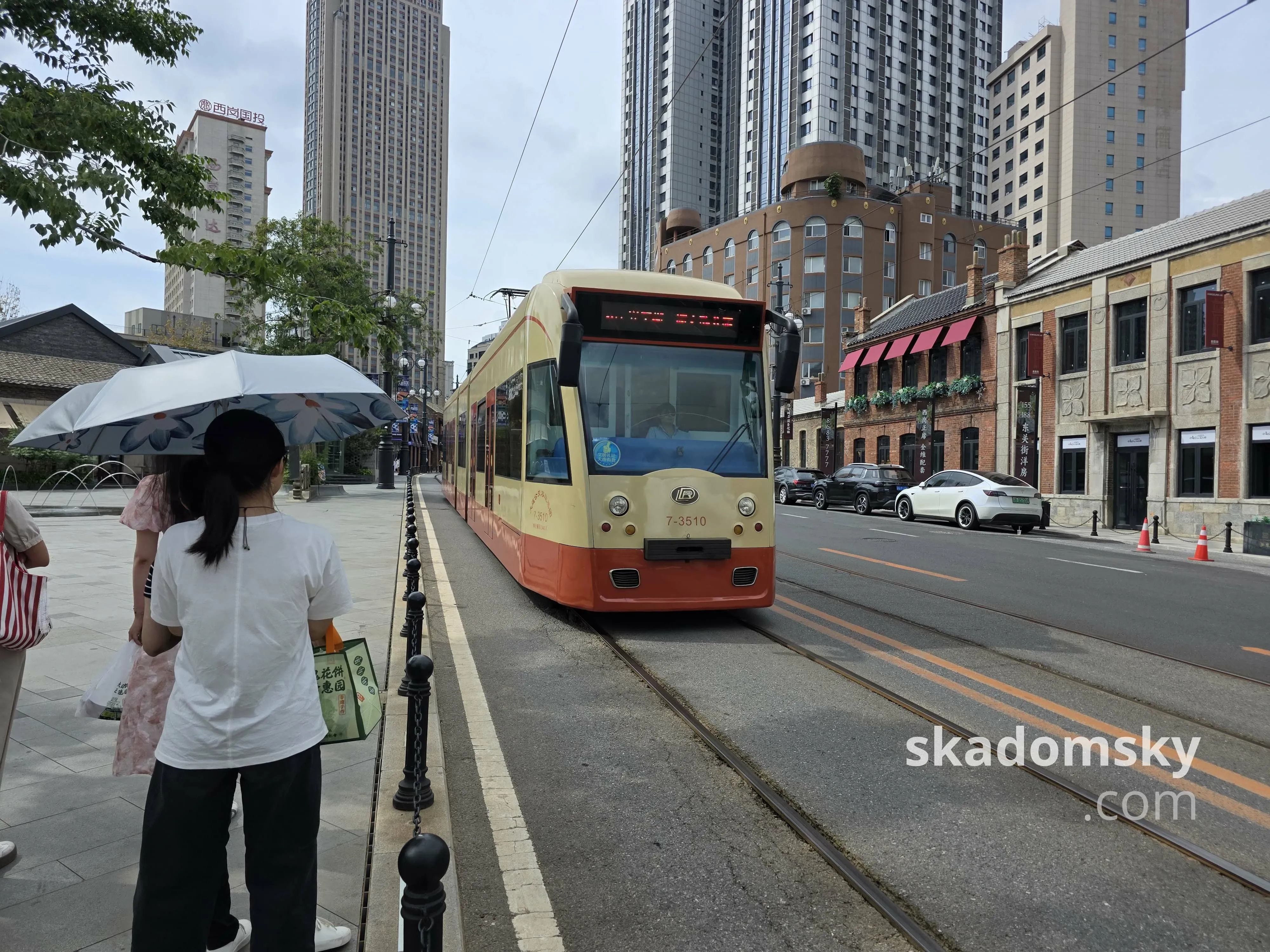 一辆三节长的黄色有轨电车贴着人行道驶来。