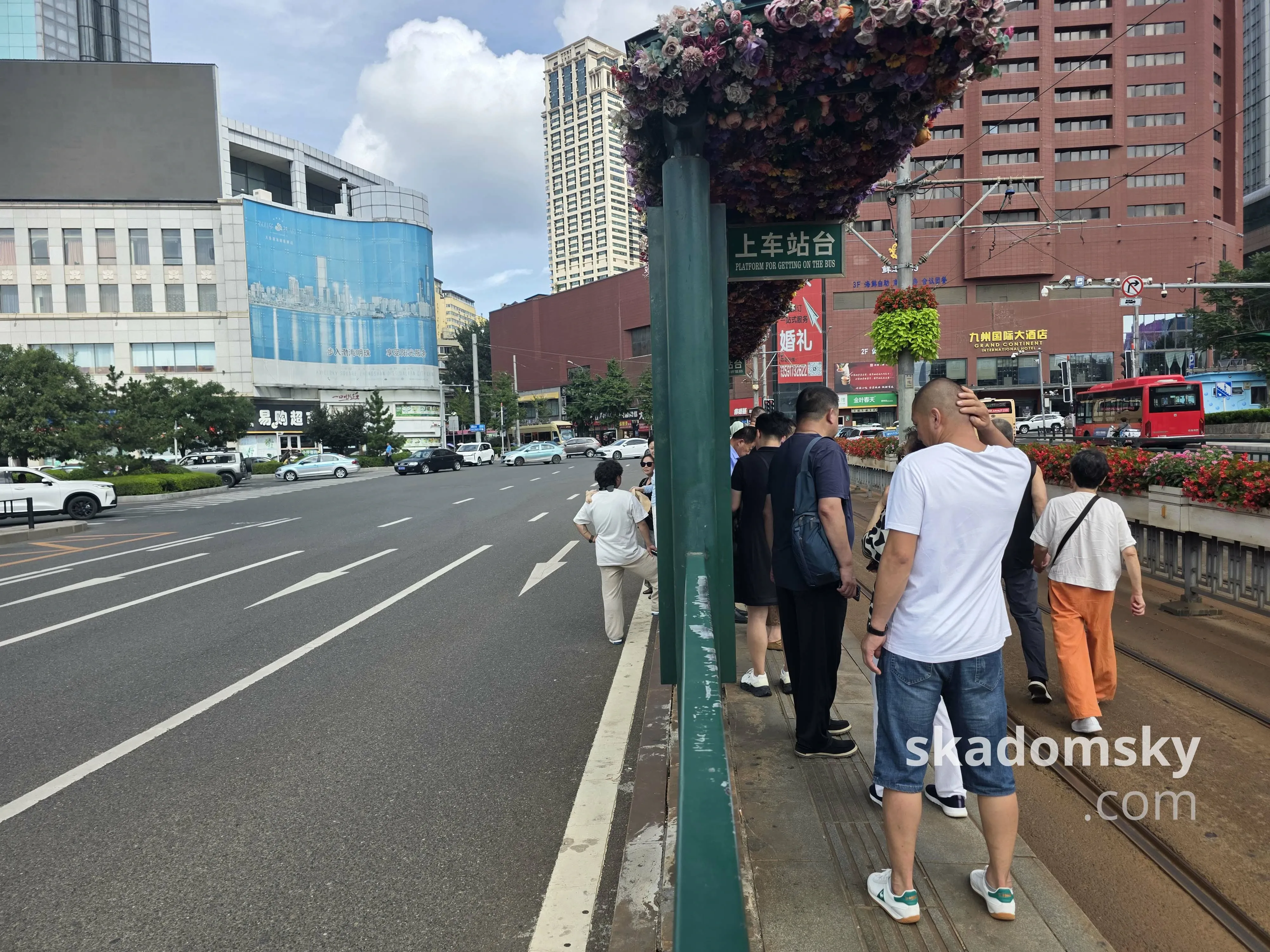 路中间有轨电车的上车站台，左侧是沥青马路，右侧是轨道区域。乘客在站台上等待。